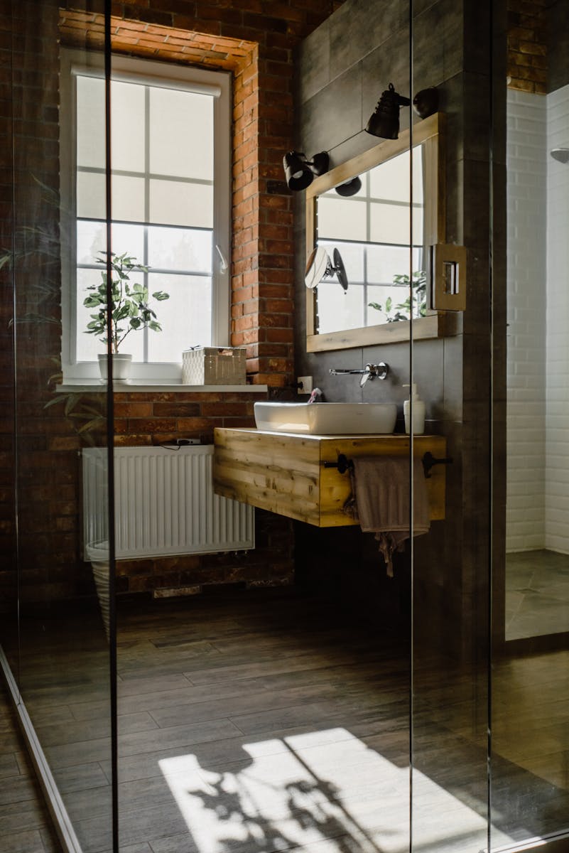 Modern bathroom with glass door, wooden sink, and natural brick wall.