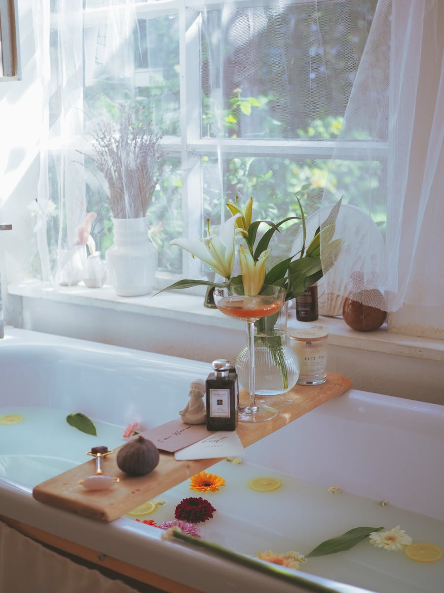 A serene bathroom with a milk bath, flowers, and elegant glass decor on a wooden tray.